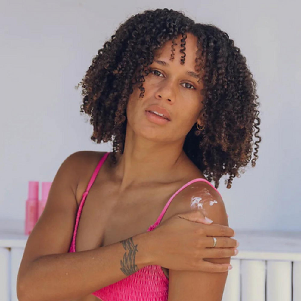 Confident woman in a pink swimsuit applying Australian made natural body care product, showcasing healthy skin and a fresh glow, embodying the beauty and vitality of Australia's premium skincare selection.