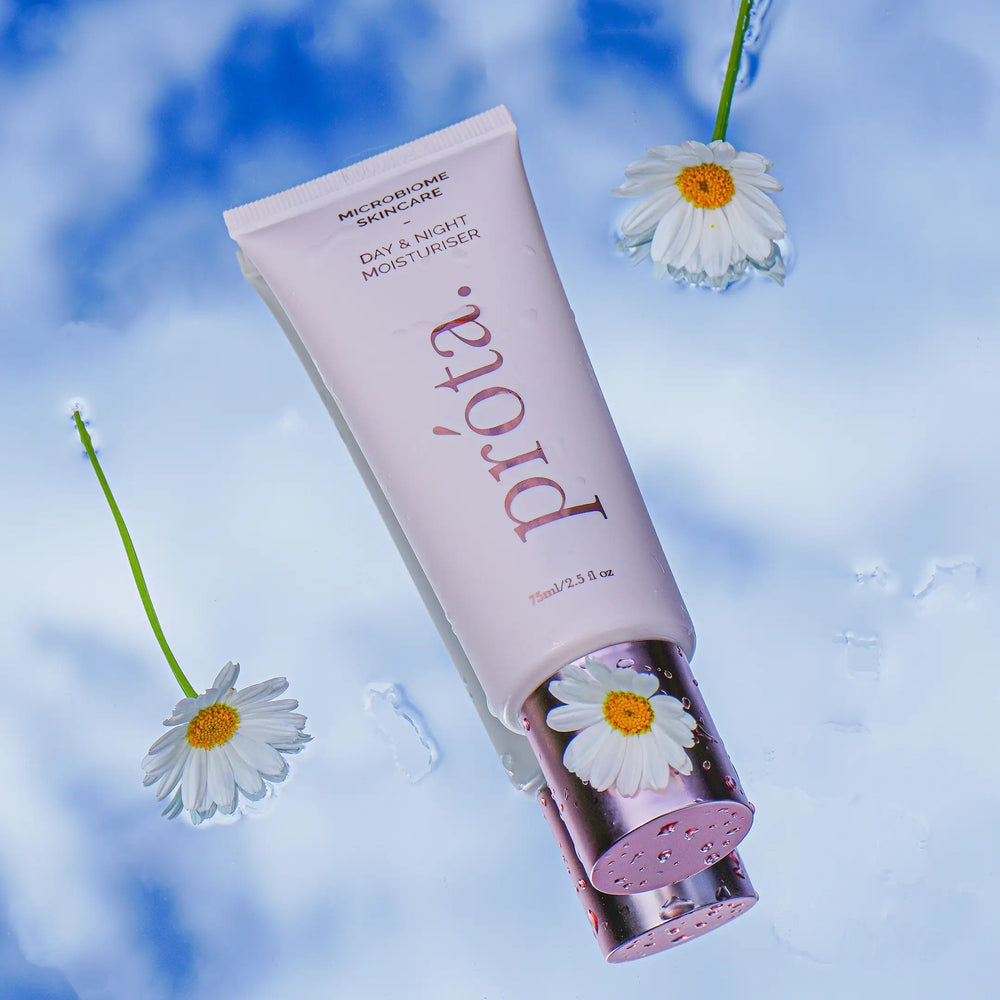 Prōta moisturizer tube floating with daisies on a reflective water surface against a cloud backdrop, embodying hydration and purity for Australian skin health.