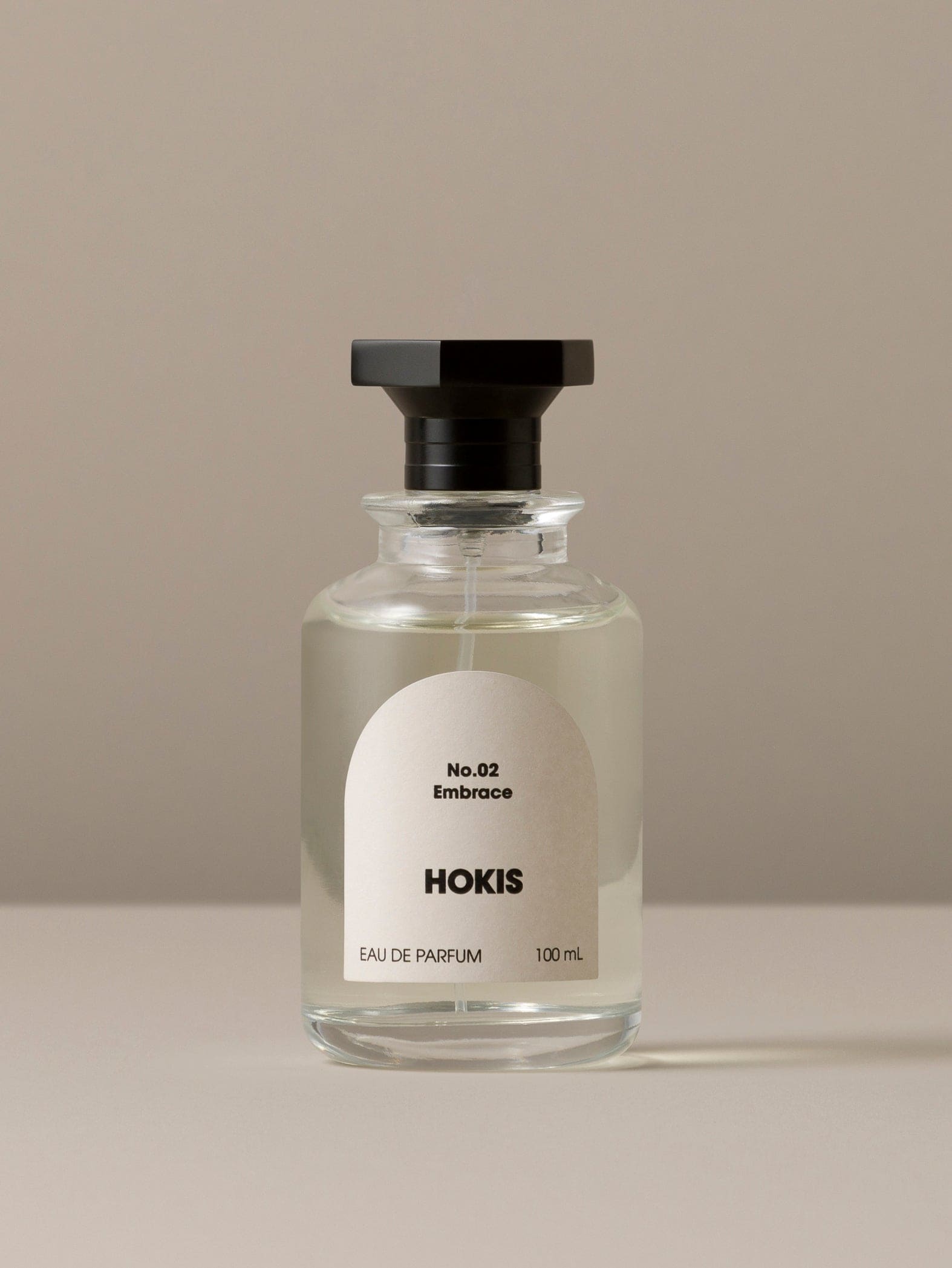 Clear glass perfume bottle with black cap and white label on a beige background