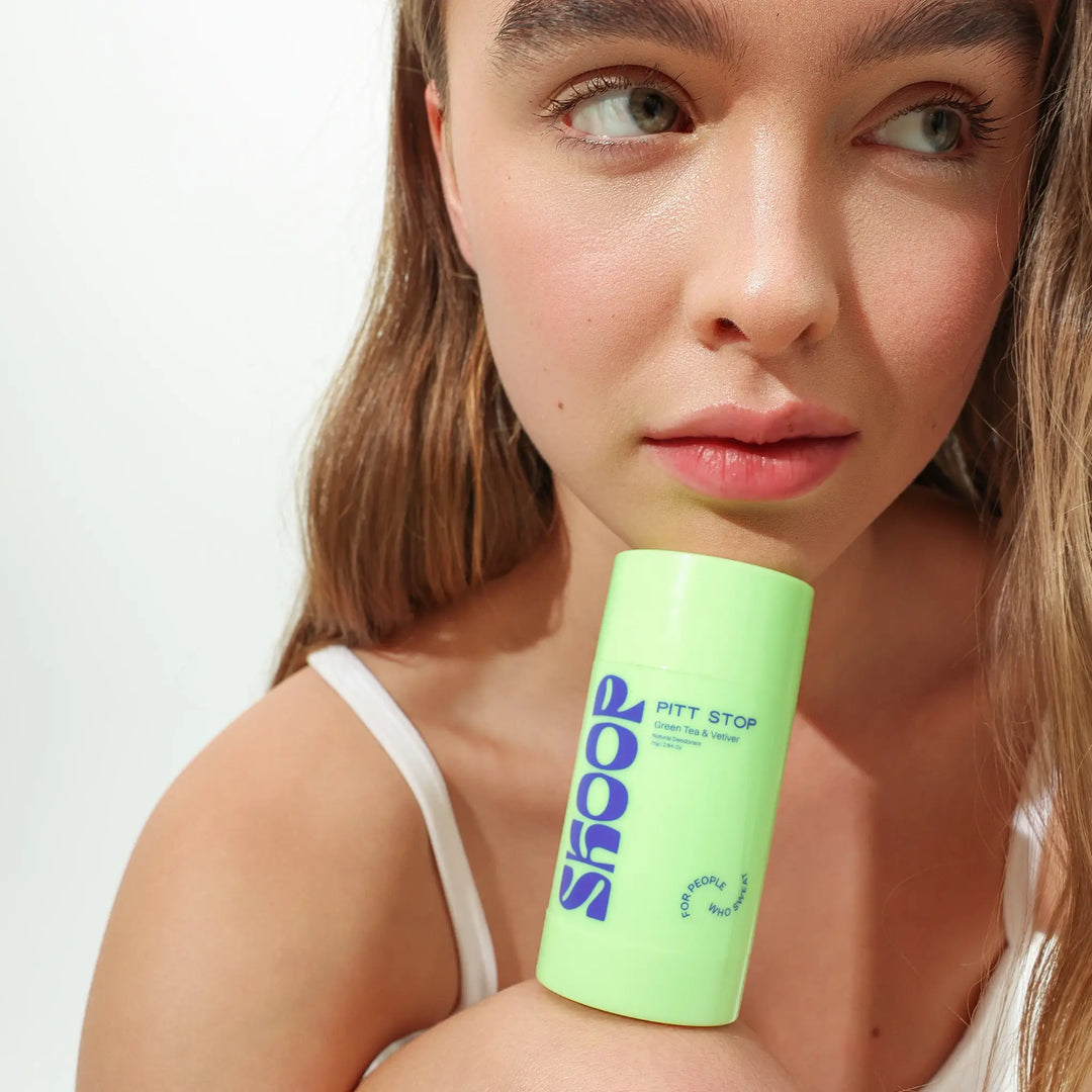 Woman holding a green best natural deodorant for women in a green roll on from Skoop Skincare product with 'Pitt Stop' branding against a white background