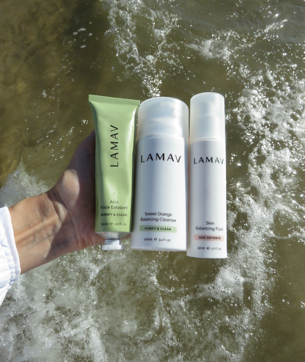 Three LAMAV skincare products held over flowing water