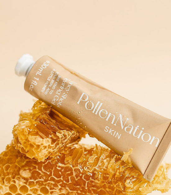An elegantly presented tube of PollenNation Skin care product, resting on a piece of natural honeycomb against a cream-colored background. The honeycomb is oozing honey, evoking the natural ingredients used in the product. This image highlights the organic and nature-inspired ethos of the skincare brand.