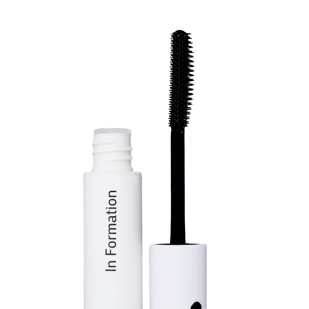 The image shows an open white cylindrical bottle labeled "In Formation. Next to the bottle is an applicator with a black wand and a spiral-bristled brush that is coated with a product, this is a hair tool. This product is for hair care, designed to tame flyaways and tame frizzy hair —this is supported by the wand's resemblance to a mascara applicator.