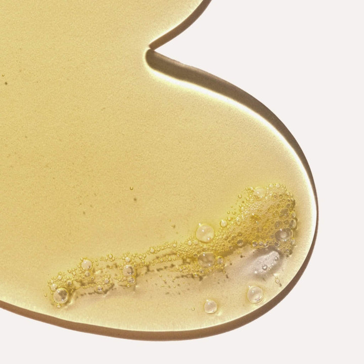 Close-up of a gold-colored all natural body wash from Saya Skincare with bubbles on a light background. Made with organic ingredients. 