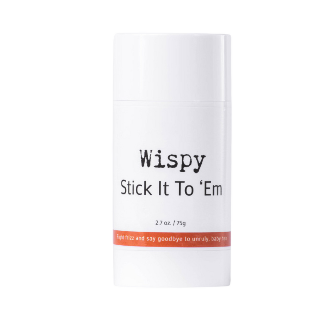 The image displays a white cylindrical container for a hair styling product named "Wispy Stick It To 'Em." It has a net weight of 2.7 oz or 75g. The label on the container features a playful and direct message, "fight frizz and say goodbye to unruly, baby hair," the product is used for smoothing and controlling frizzy hair and flyaways. This is a hair wax stick.