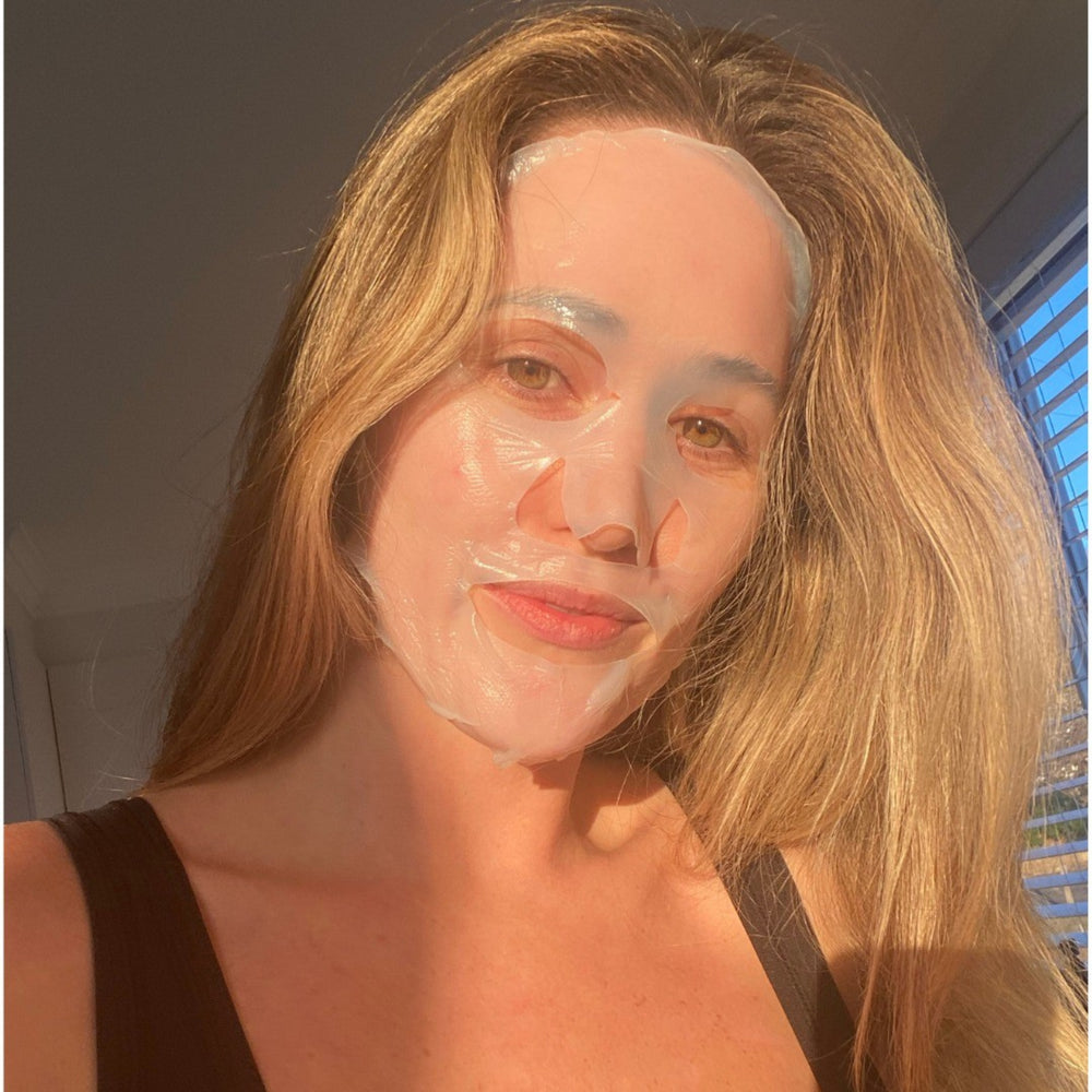Woman with a bio-cellulose sheet mask on her face, sunlit room with blinds casting shadows, symbolizing self-care and beauty rituals in Australia.