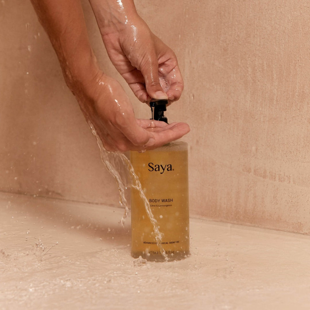 Hand holding a bottle of Saya Skincare all natural body wash under running water.