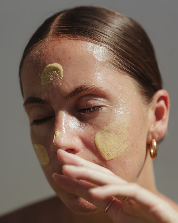 Woman applying best face cleanser for acne prone skin to her face with a neutral background