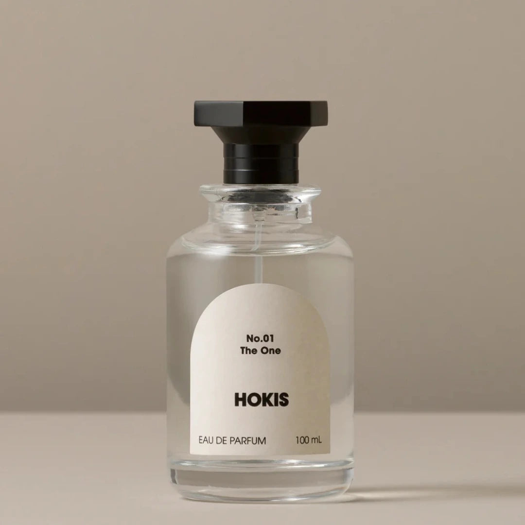 Clear glass perfume bottle with black cap and white label on a beige background