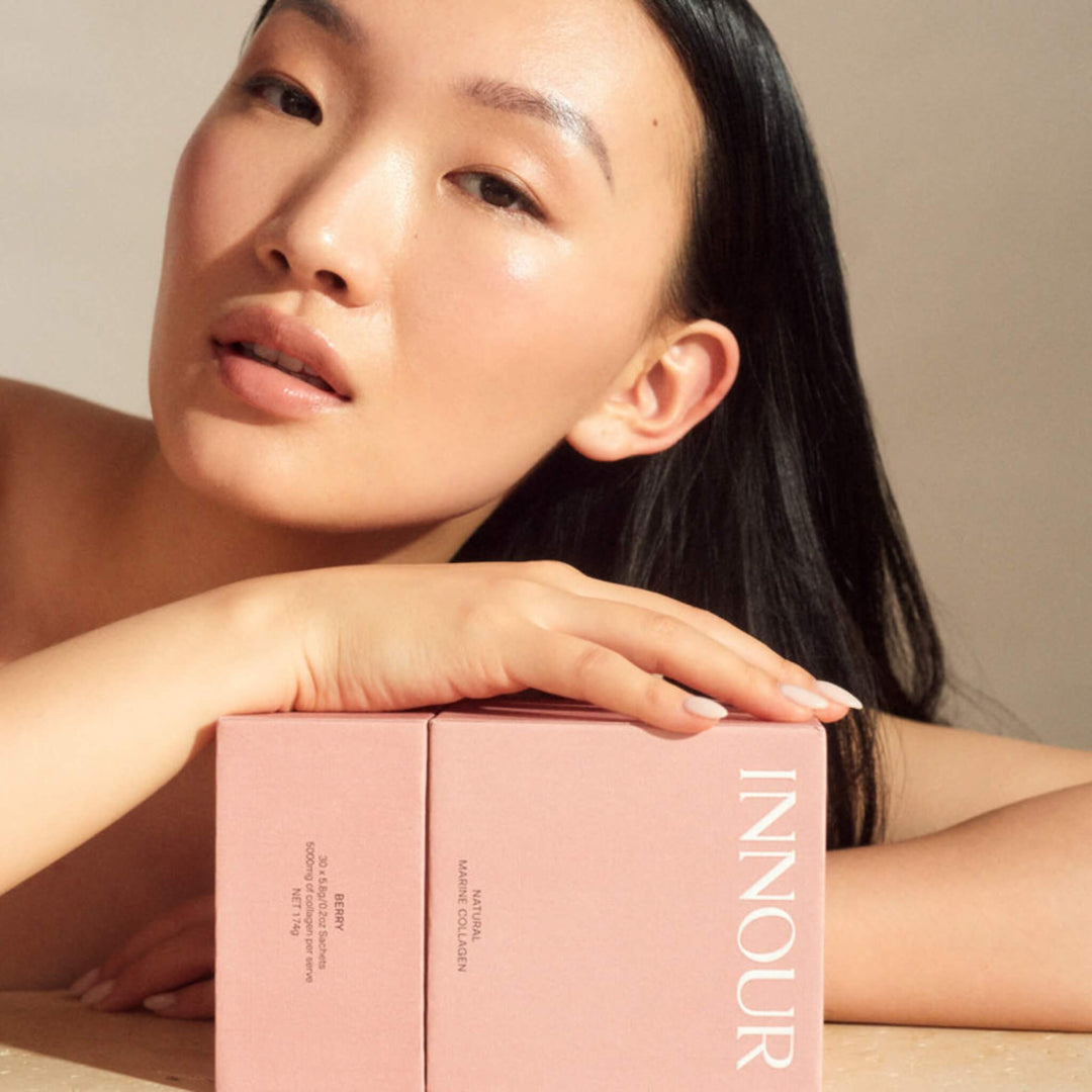 Woman holding a pink marine collagen powder for glowing skin INNOUR product box against a neutral background