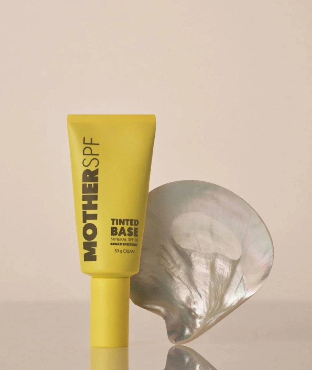 Yellow tube of MOTHER SPF tinted sunscreen base on a beige background