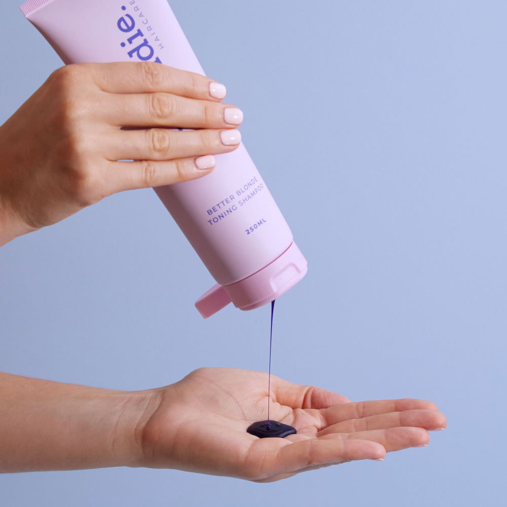 Hand holding Brondie Haircare's Better Blonde toning shampoo tube with a dollop of purple product for maintaining blonde tones.