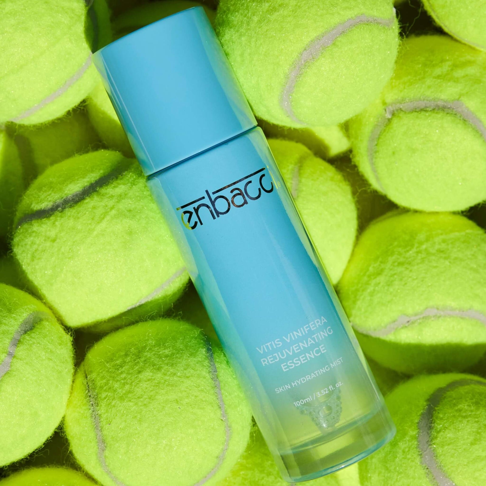 Enbacci Vitis Vinifera Rejuvenating Essence surrounded by tennis balls, antioxidant mist toner with grape stem cells for daily hydration