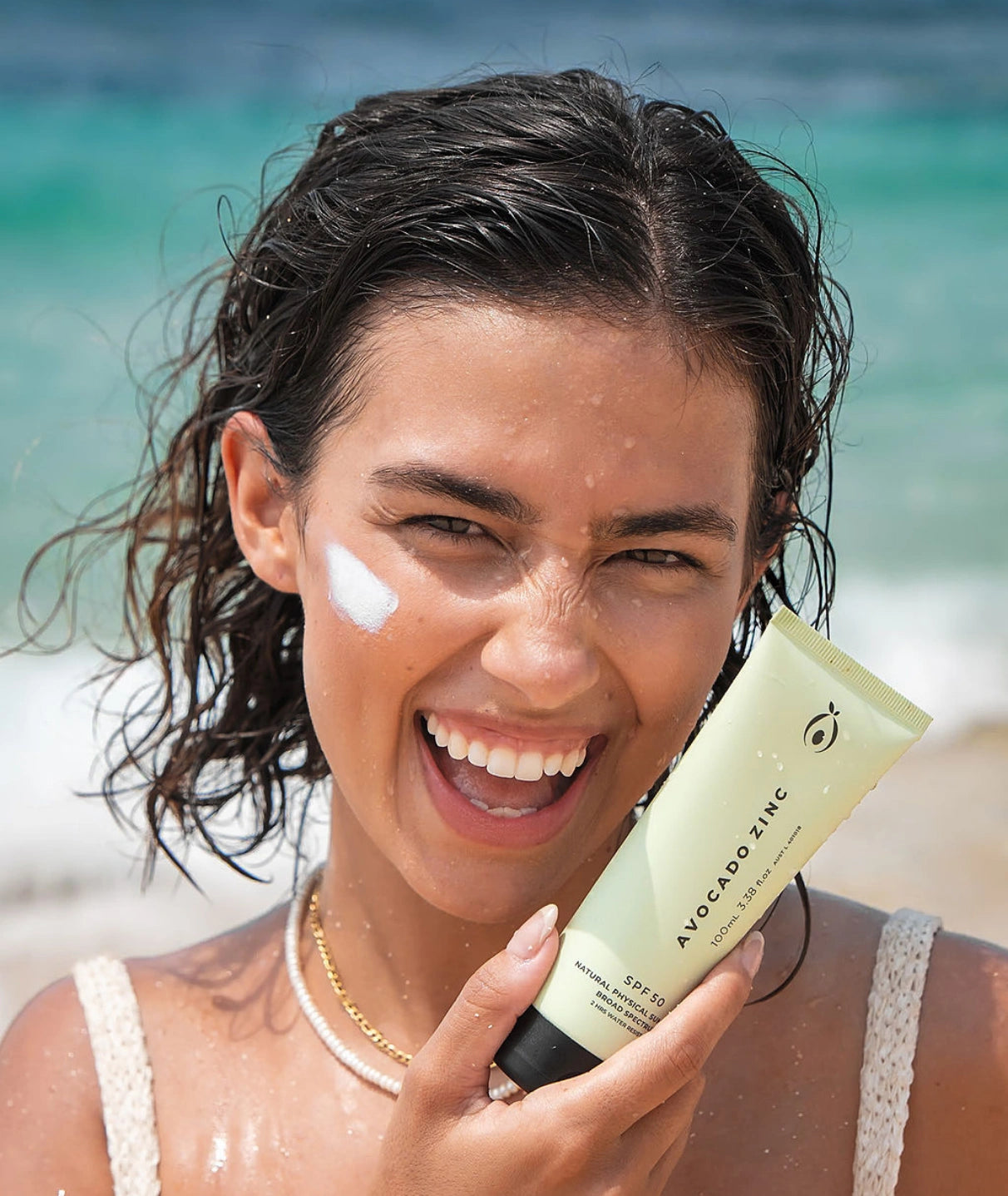 Woman applying mineral  sunscreen on a beach with a bottle of Avocado Zinc visible