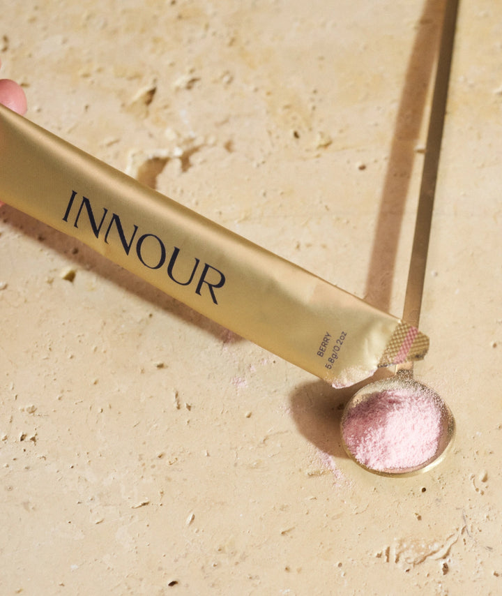 Hand holding an Innour Berry marine collagen sachet pouring into a gold spoon.