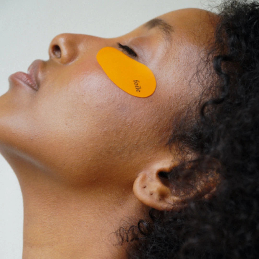 Person with an orange silicone eye pads on their face against a white background