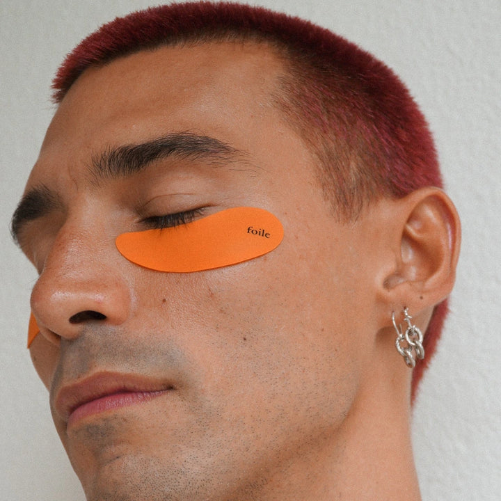 Man with orange silicone eye pads labeled 'foile' on a neutral background