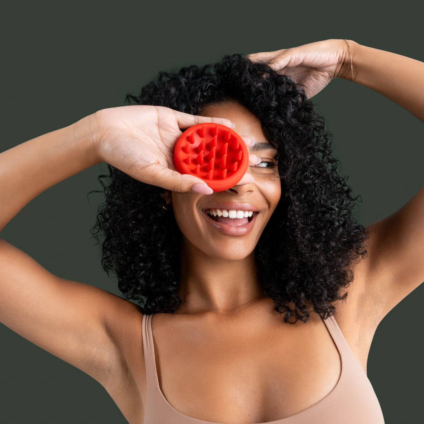 Smiling woman with curly hair holding OVEV Wellness red scalp scrubber, promoting hair growth and scalp care for all hair types.