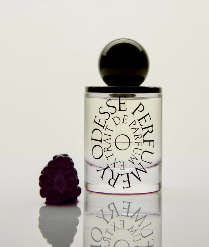 Odesse Hotel Jasmine Extrait de Parfum luxury perfume bottle with black spherical cap beside fresh blackberry on a reflective surface, featuring notes of jasmine, blackberry, saffron and cream fragrance.