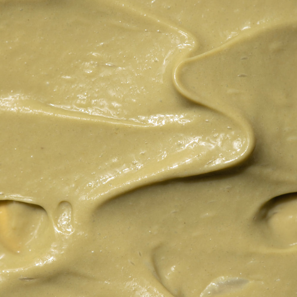 A close-up image of a Australian certified organic, textured face scrub in a pale green hue spread across a surface, creating a creamy texture.