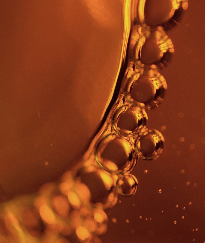 Macro photography of golden amber liquid bubbles representing natural perfume oil.