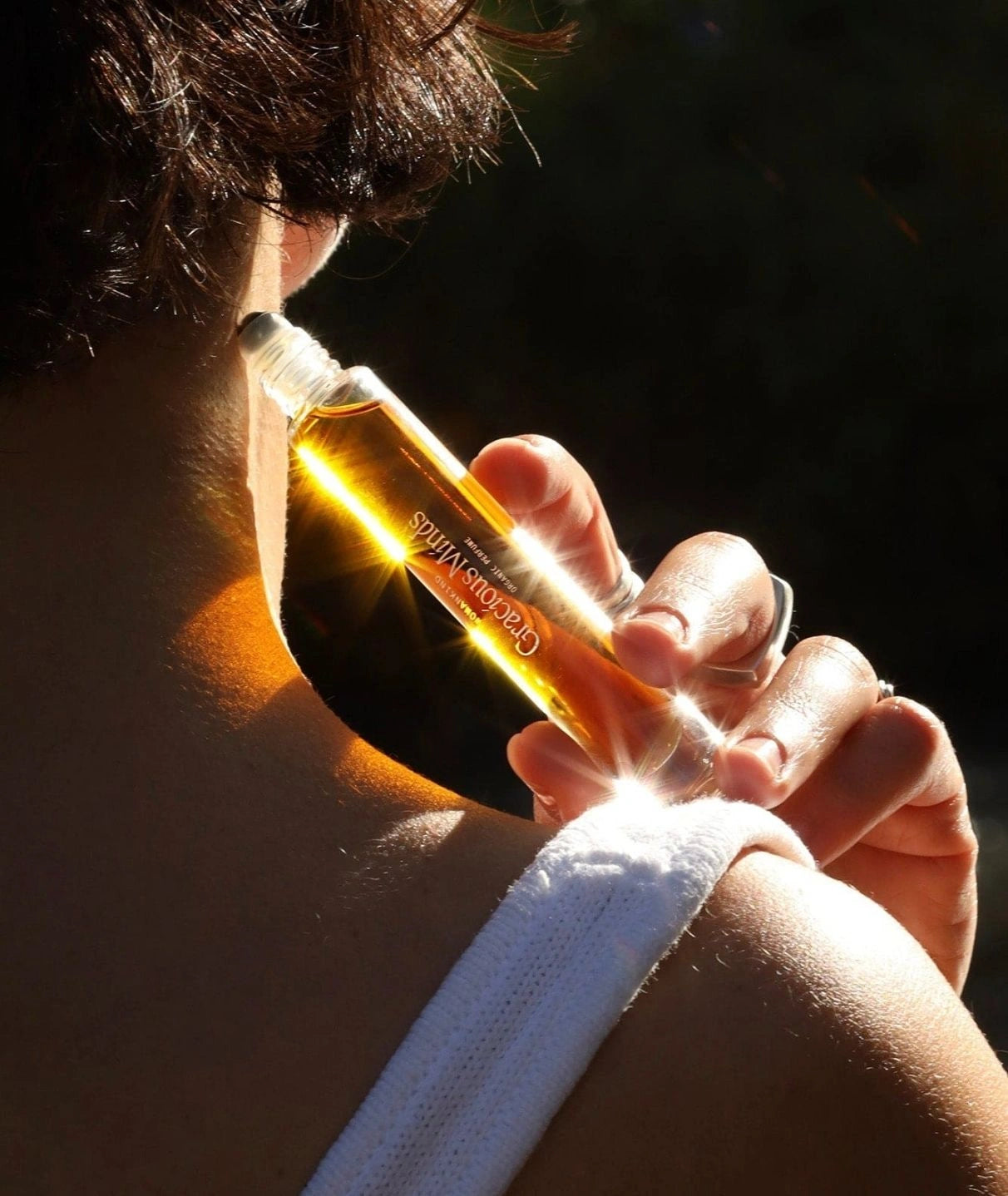 Woman applying Gracious Minds Womankind organic roll-on perfume to their neck.