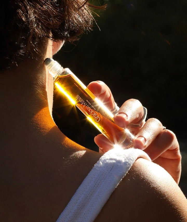 Woman applying Gracious Minds Womankind organic roll-on perfume to their neck.