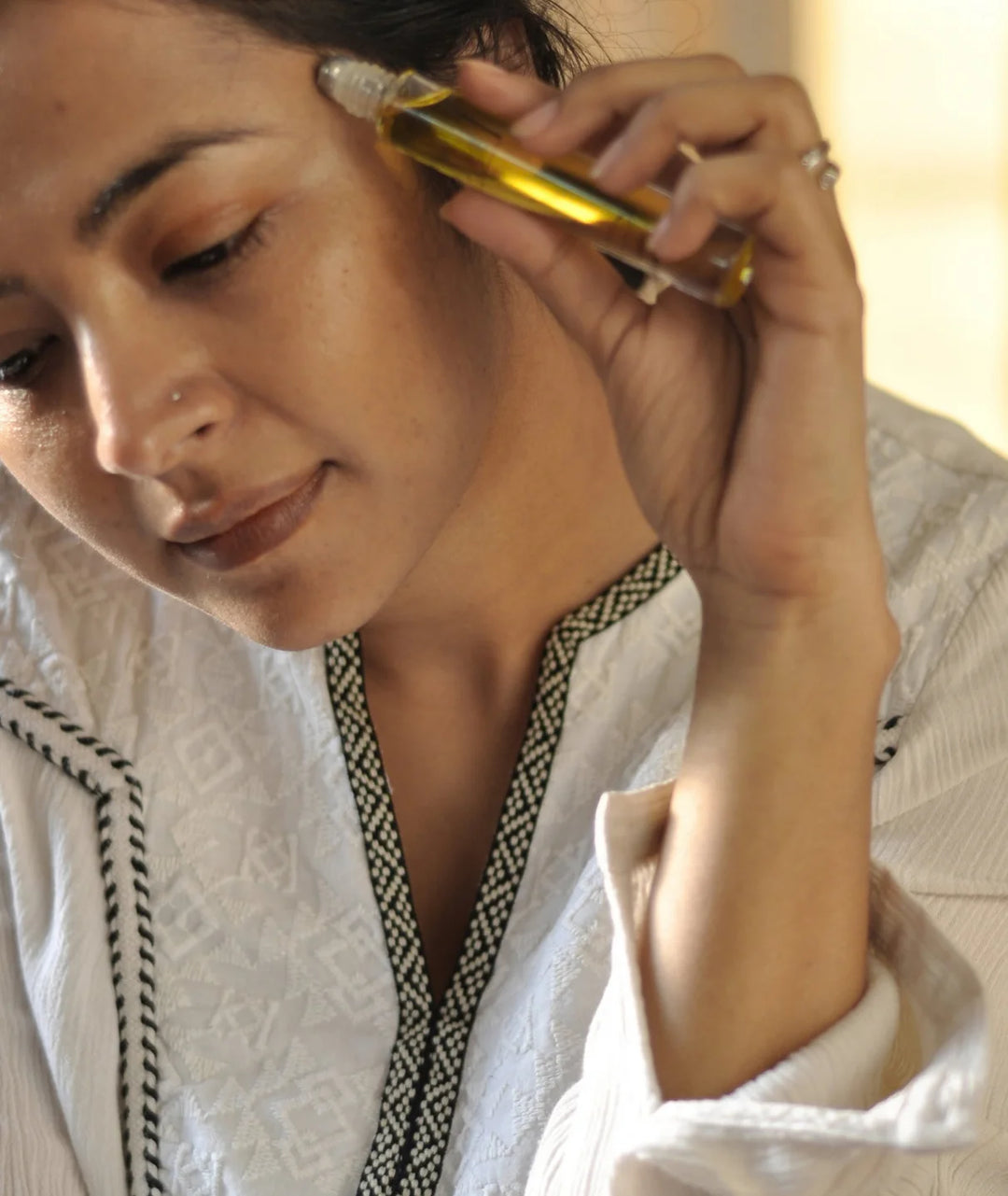 Woman applying Serene Bodyhealth Ground essential oil perfume rollerball to her temple