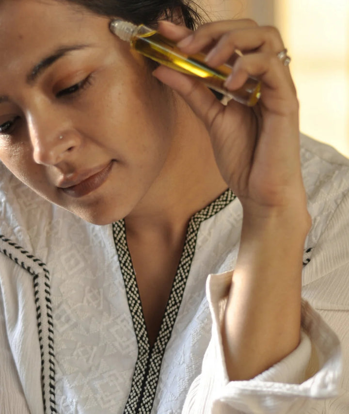 Woman applying Serene Bodyhealth Ground essential oil perfume rollerball to her temple