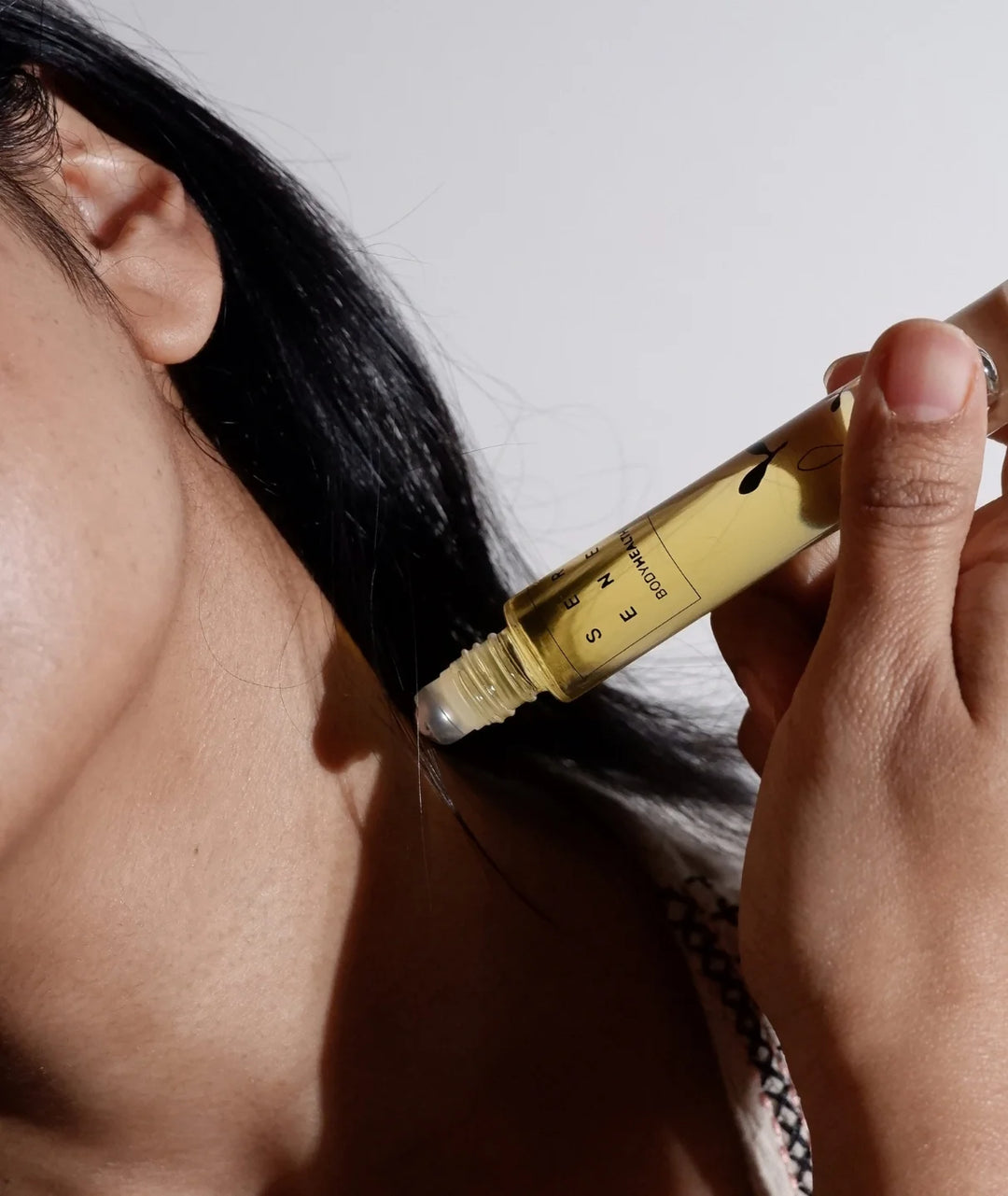 Close-up of applying Serene Bodyhealth essential oil perfume rollerball near the neck.