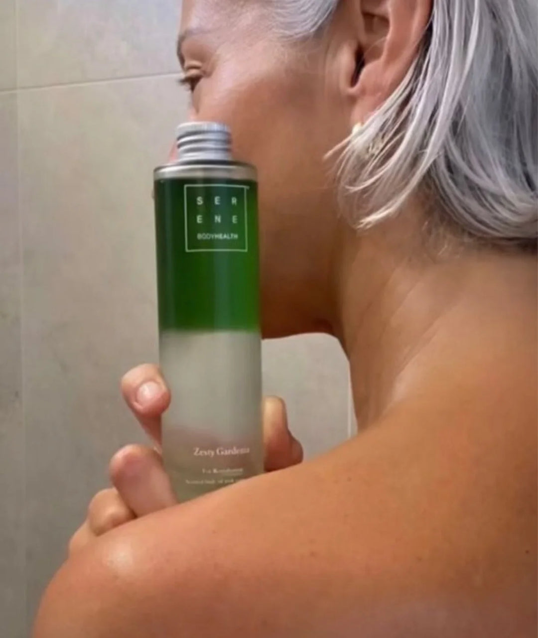 Woman holding Serene Bodyhealth Zesty Gardenia scented magnesium body oil against her shoulder.