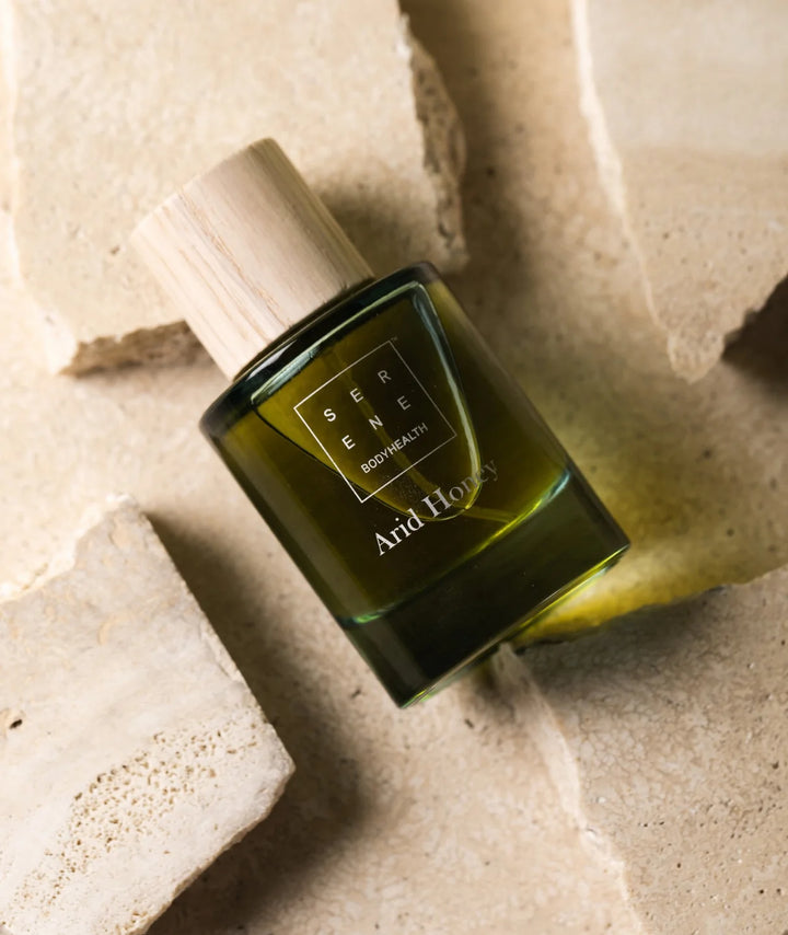 Arid Honey fragrance by Serene Bodyhealth with wooden cap resting on textured beige stone slabs.