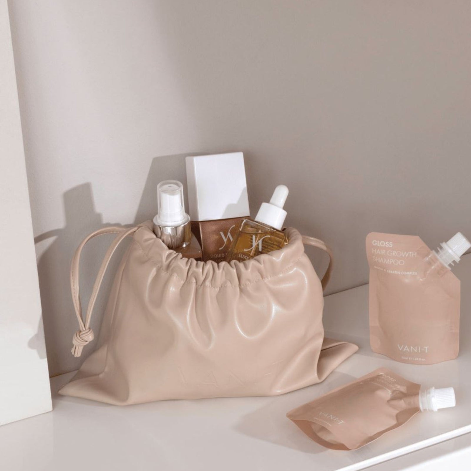 Elegant drawstring beauty bag in a soft nude shade, filled with skincare and haircare essentials, including serums, sprays, and VANI-T Gloss Hair Growth Shampoo sachets. Styled on a minimal vanity, this modern storage solution is perfect for organising beauty products with ease and sophistication.
