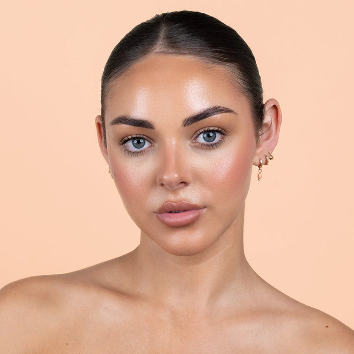 Woman bronzing drops for face from Avocado Zinc on a peach background