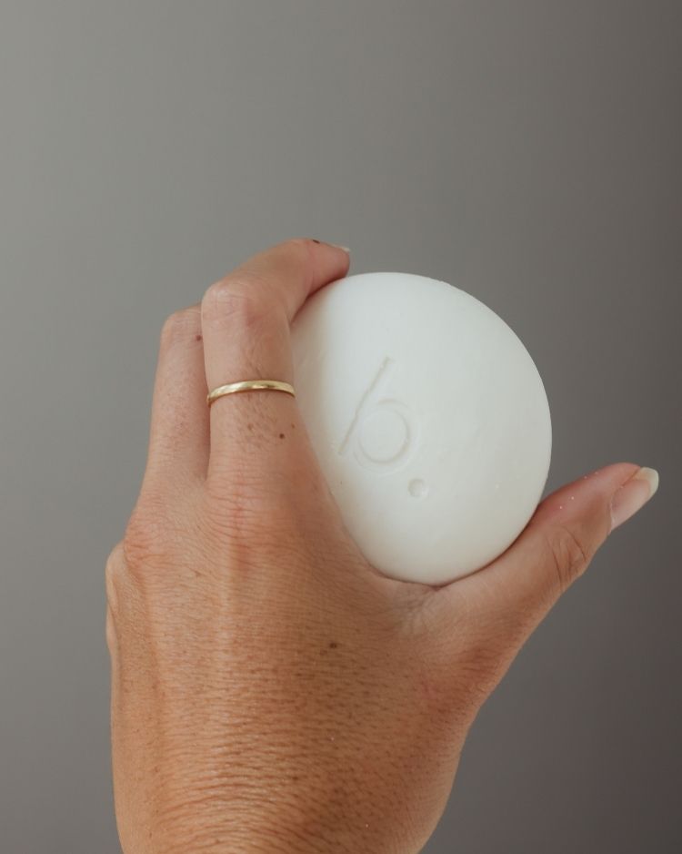 Hand holding a white face wash for sensitive combination skin with a brand logo against a gray background