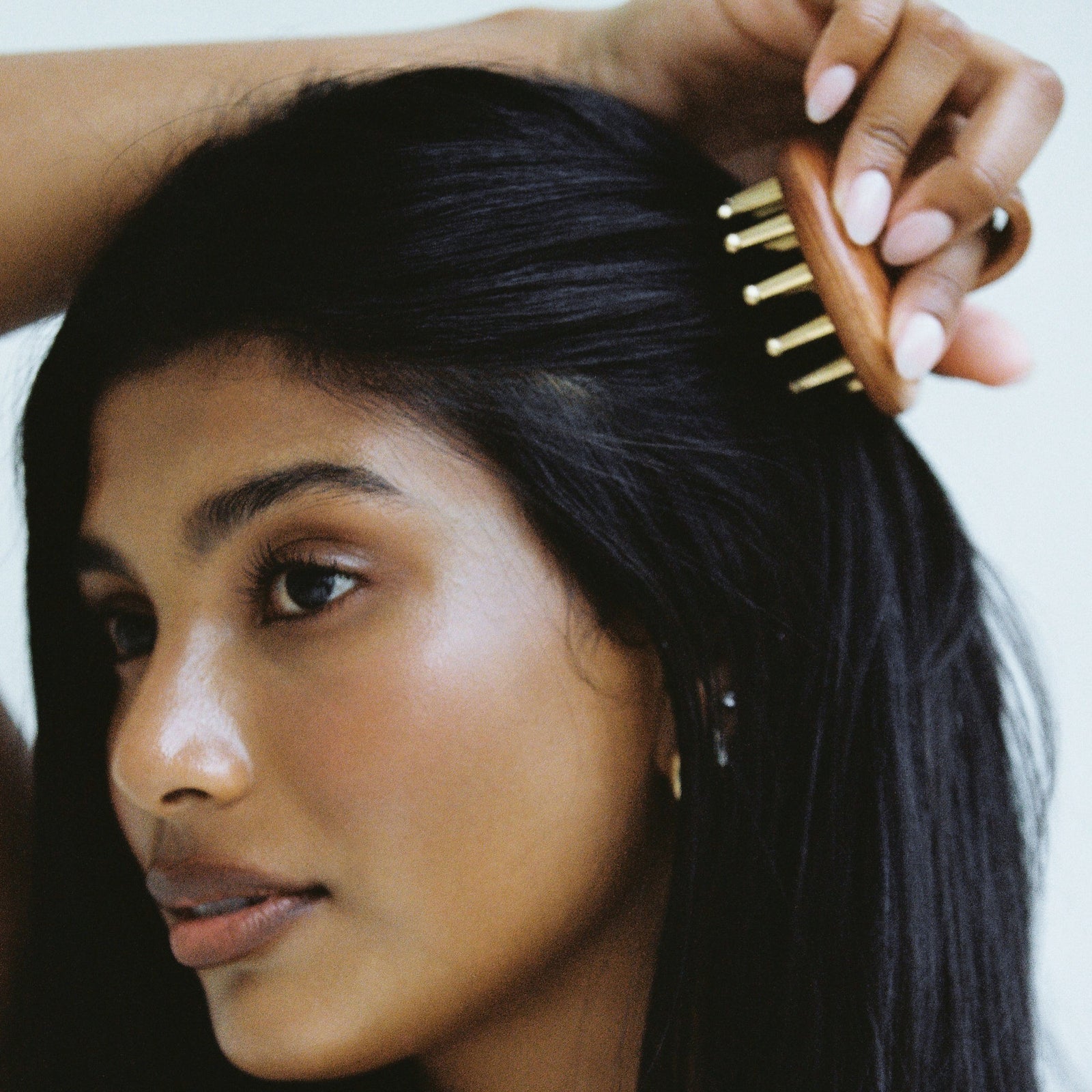 Model using a wooden hair massager with copper bristles to stimulate the scalp, an Ayurvedic beauty product known to improve hair health and reduce hair loss. Available at VAMS Beauty, offering natural beauty tools inspired by holistic wellness.