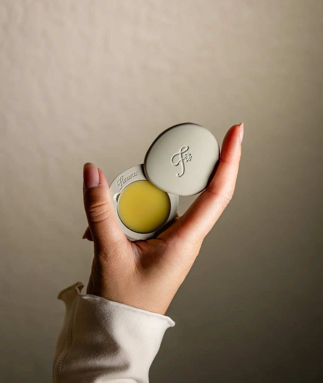 Fleurac Forest Fig Solid Perfume — Hand holding open pebble compact revealing solid perfume balm