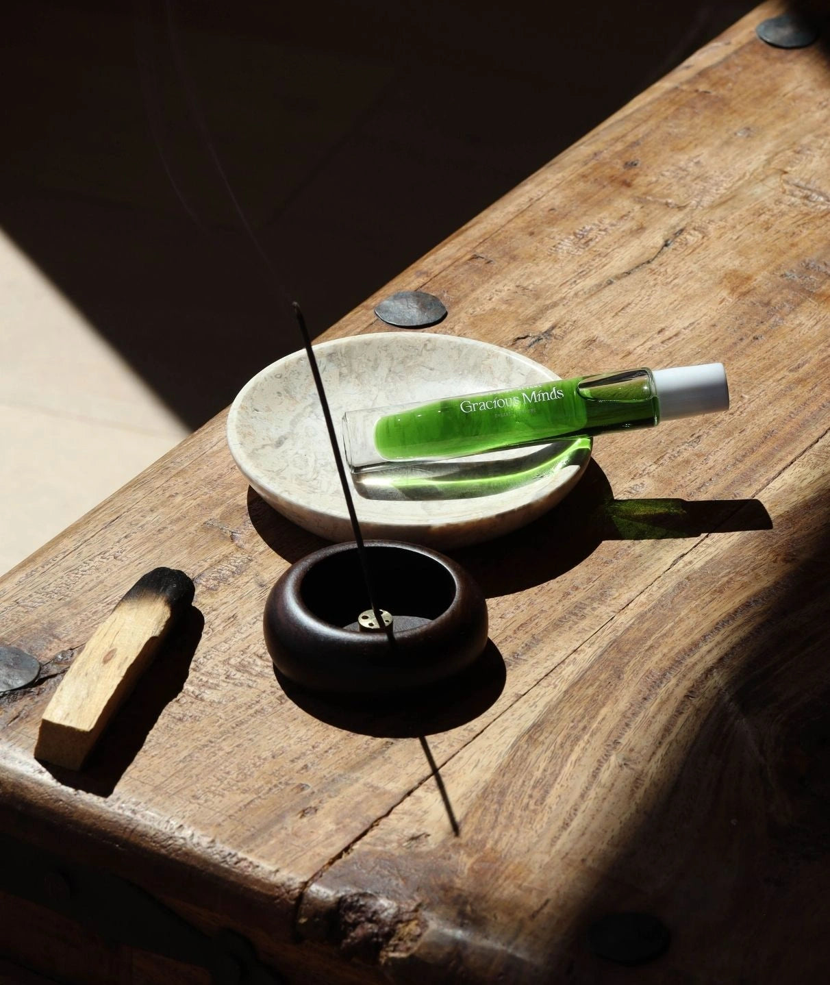 Gracious Minds organic roller perfume on a marble dish with palo santo and incense.