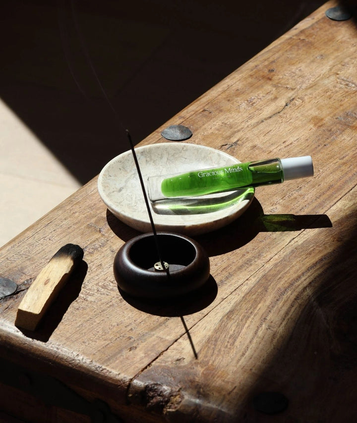 Gracious Minds organic roller perfume on a marble dish with palo santo and incense.