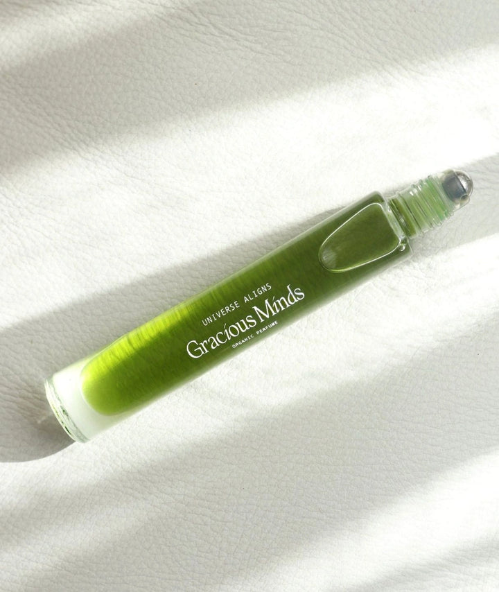 Close up of Gracious Minds Universe Aligns organic green rollerball perfume on a white surface.
