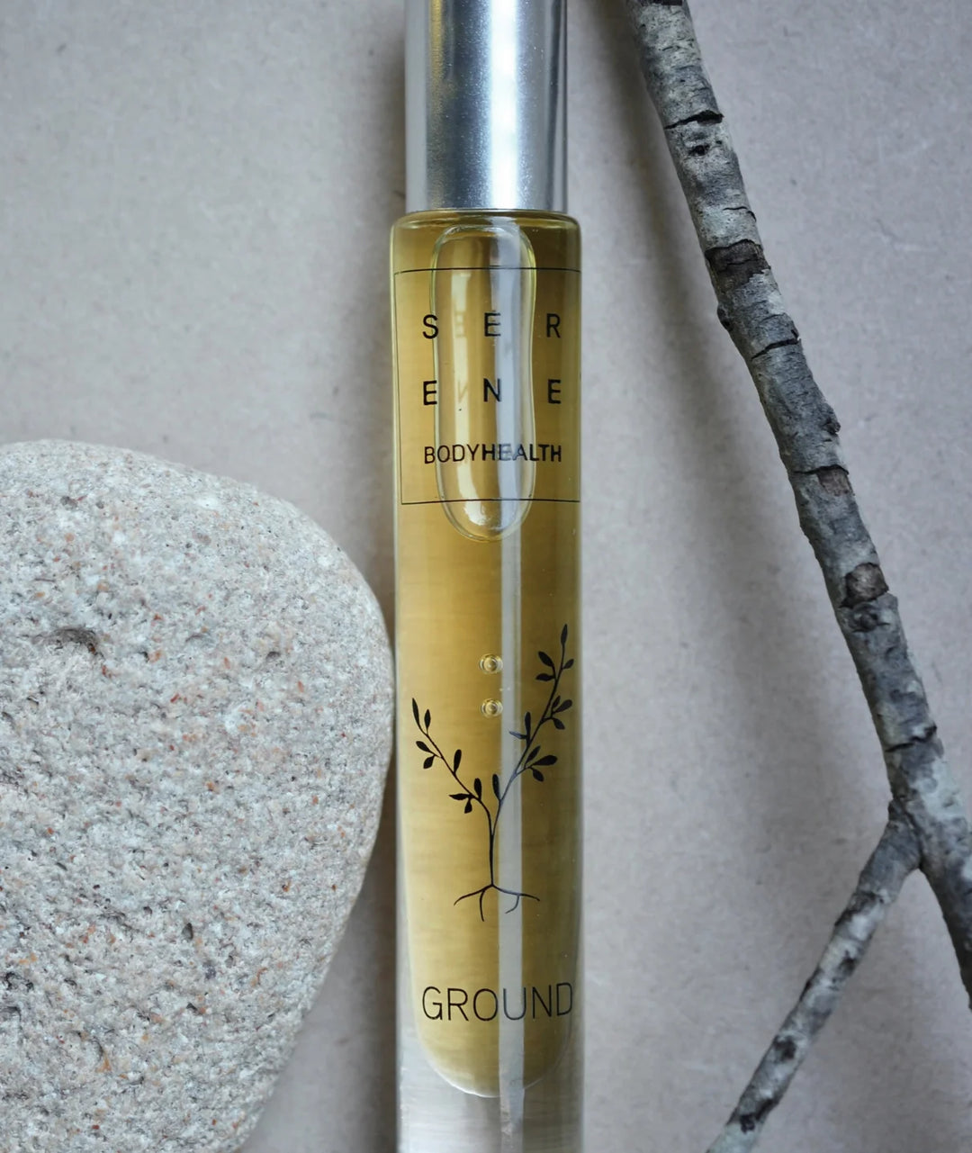 Serene Bodyhealth Ground essential oil rollerball bottle styled with a rock and tree branch