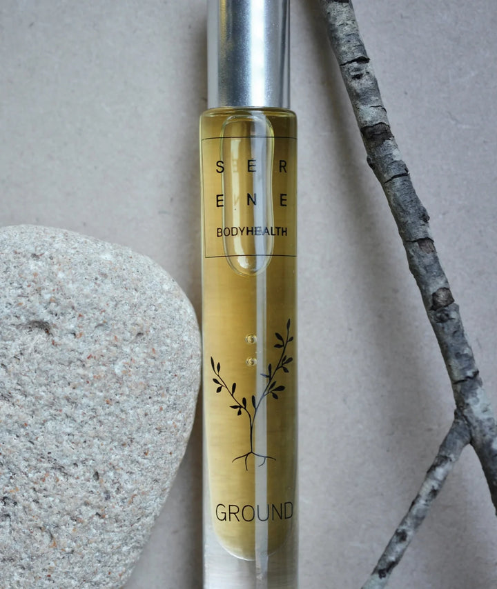 Serene Bodyhealth Ground essential oil rollerball bottle styled with a rock and tree branch
