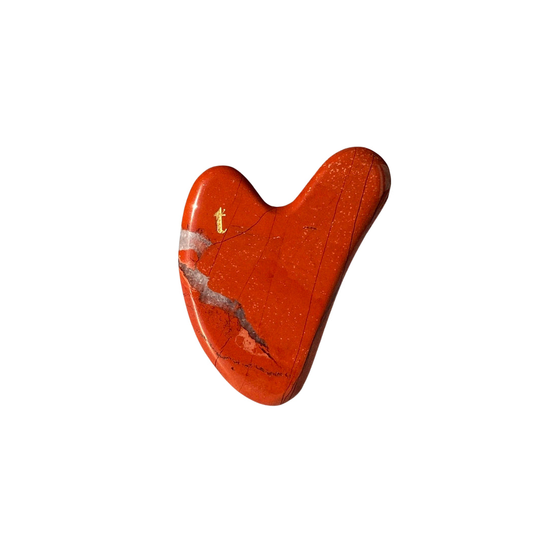 Vibrant red gua sha stone with natural veining, engraved with a golden 'T', it’s an anti-aging skincare tool available at an Australian online beauty shop Vams Beauty.