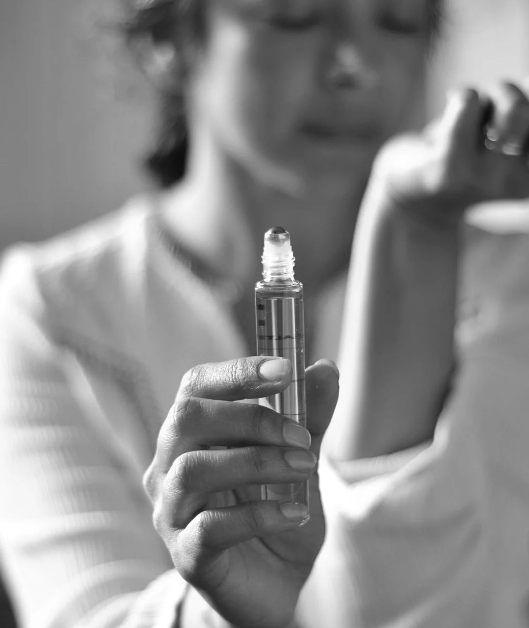 Black and white close-up of hand holding Serene Bodyhealth Ground essential oil perfume rollerball.