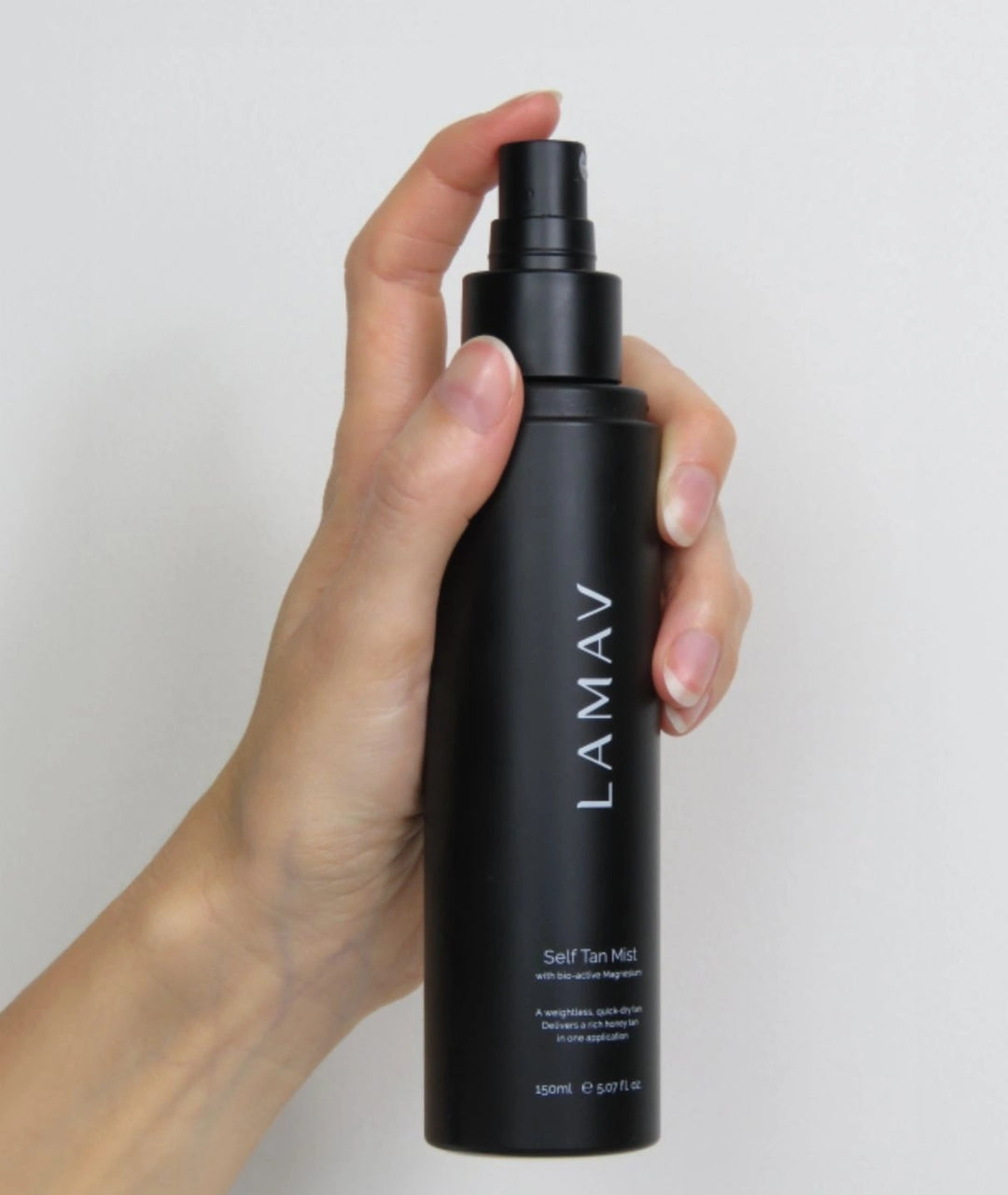 Hand holding and spraying the LAMAV Self Tan Mist bottle against a white background.