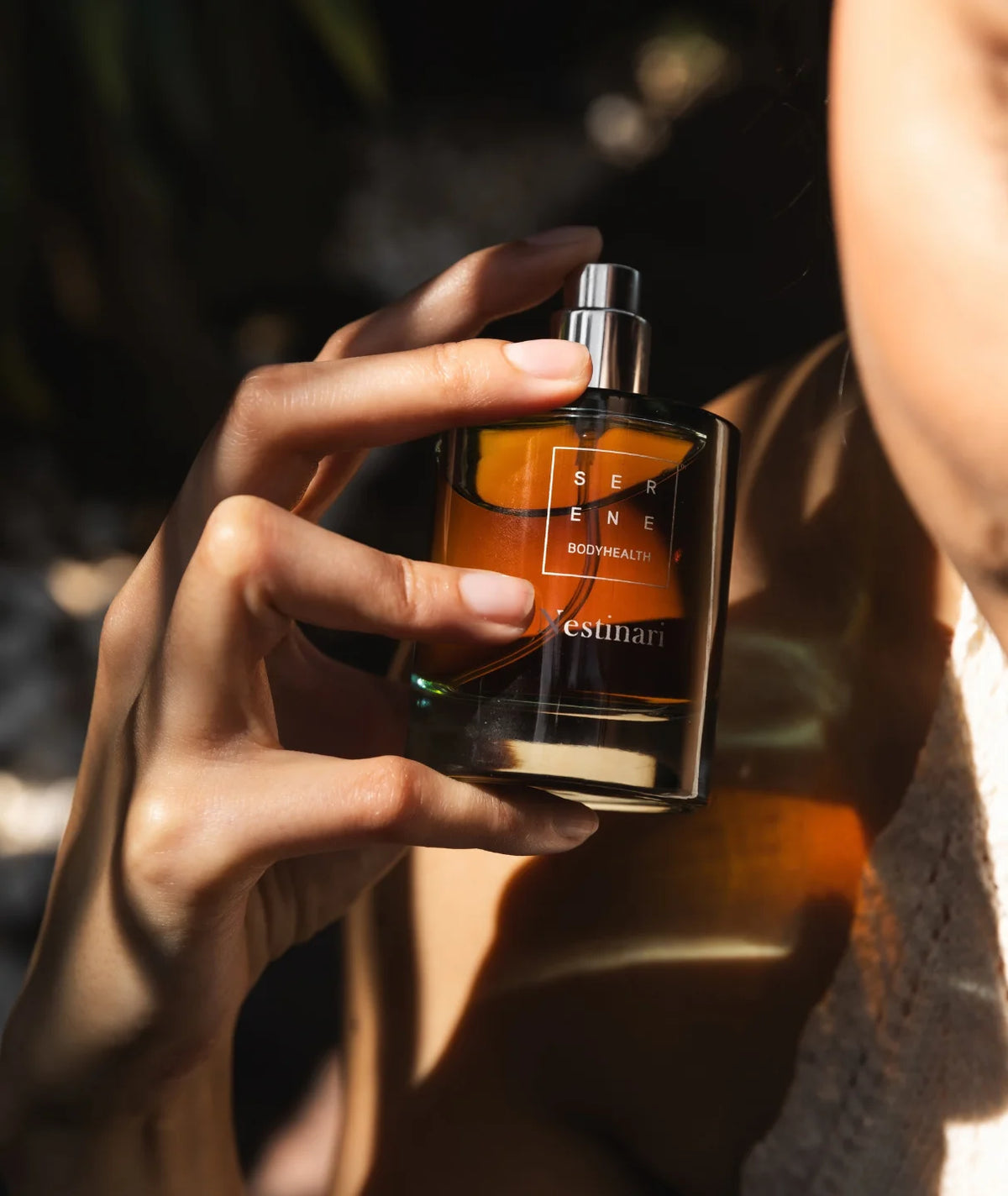 Hand holding open Serene Bodyhealth Nestinari perfume bottle with spray nozzle in sunlight.