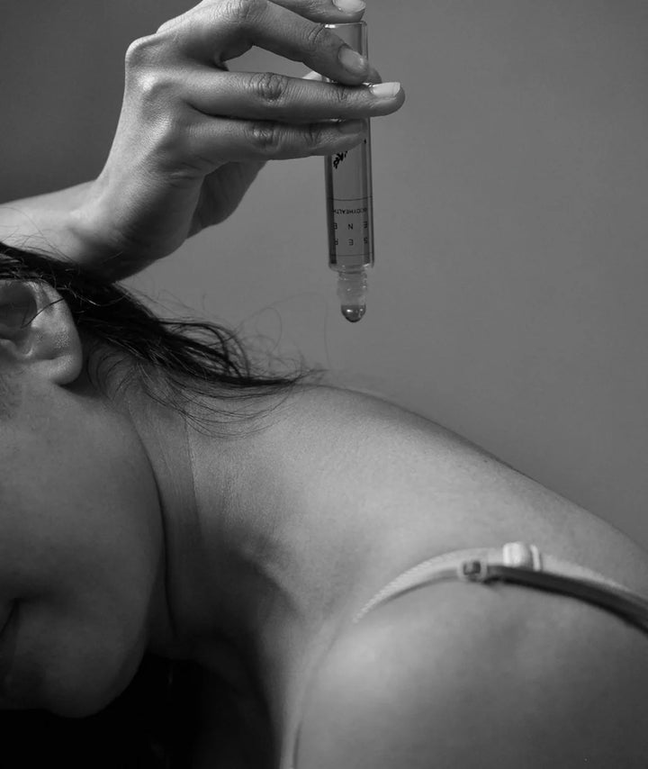 Hand holding Serene Bodyhealth Rest essential oil rollerball above shoulder in black and white.