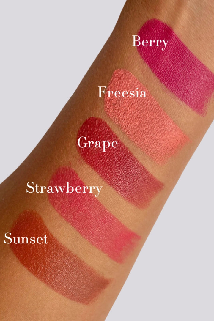 Lipstick swatches on a arm labeled 'Berry', 'Freesia', 'Grape', 'Strawberry', and 'Sunset' against a neutral background.