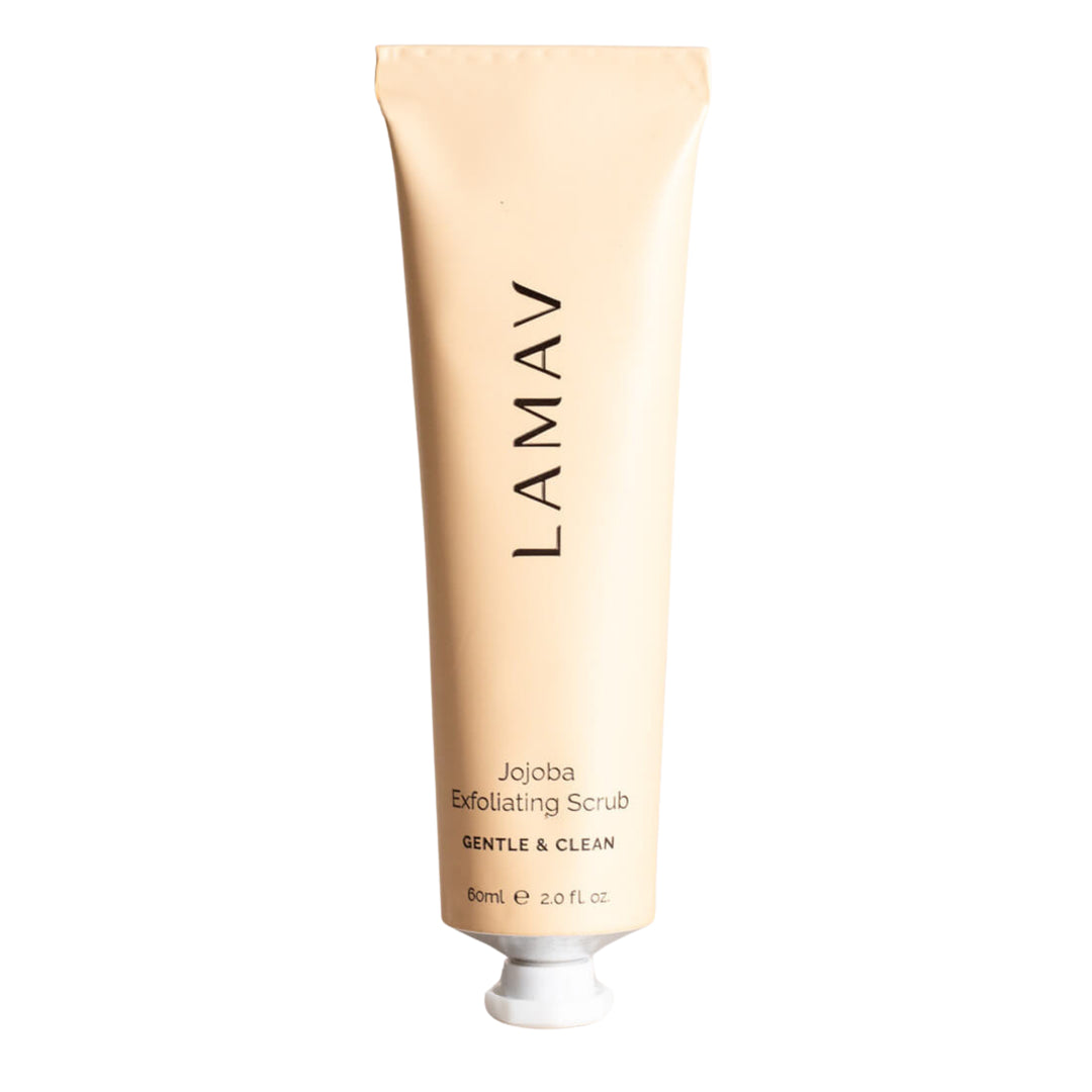 A tube of LAMAV Jojoba Exfoliating Scrub in a soft beige color with black text, standing upright on a white background. It is labelled 'GENTLE & CLEAN' and has a net weight of 60ml or 2.0 fl oz. The packaging's simple and elegant design suggests a natural and organic skincare product.