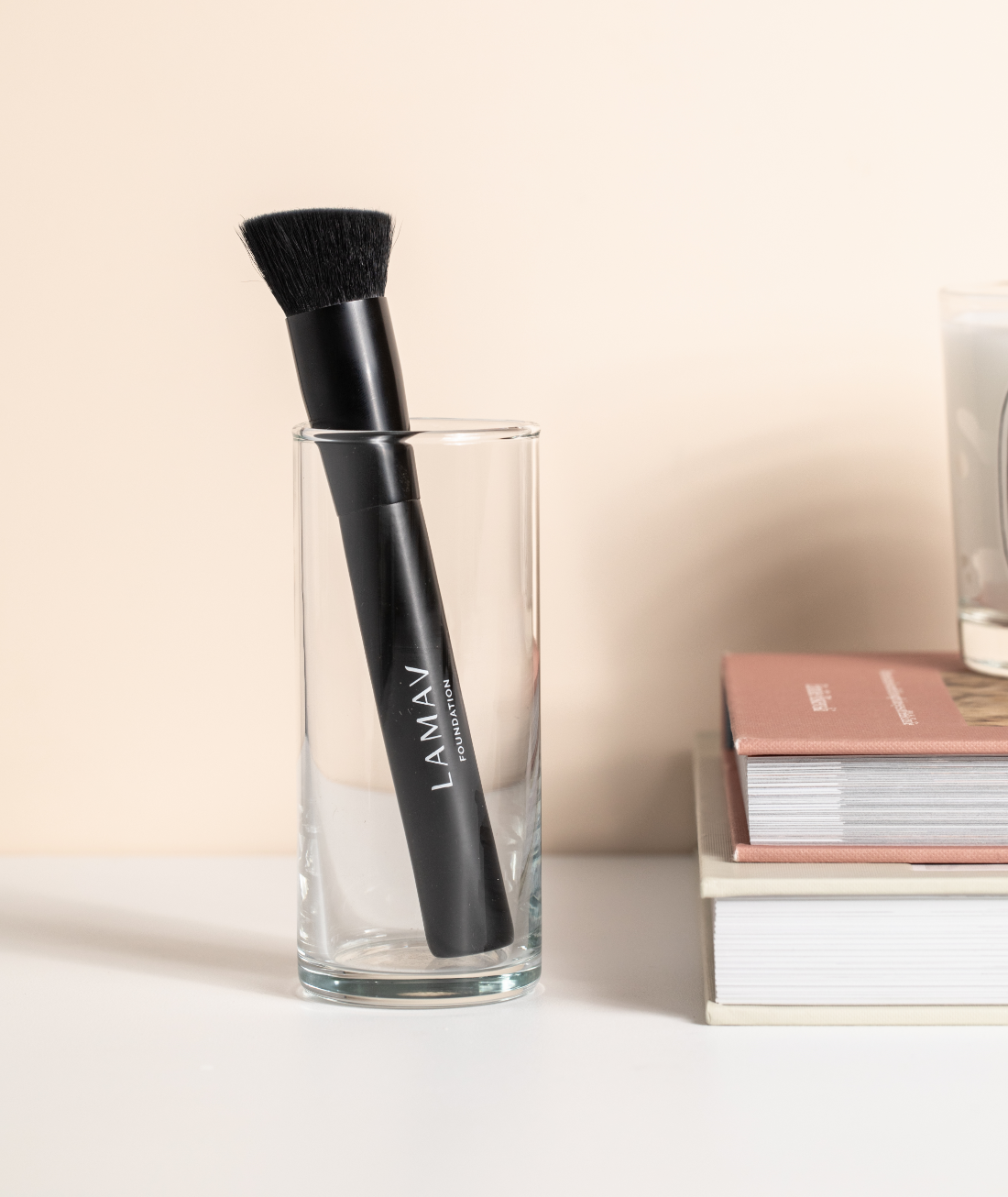 LAMAV Vegan Foundation Brush resting in a glass cup next to books. Angled makeup brush for seamless blending.